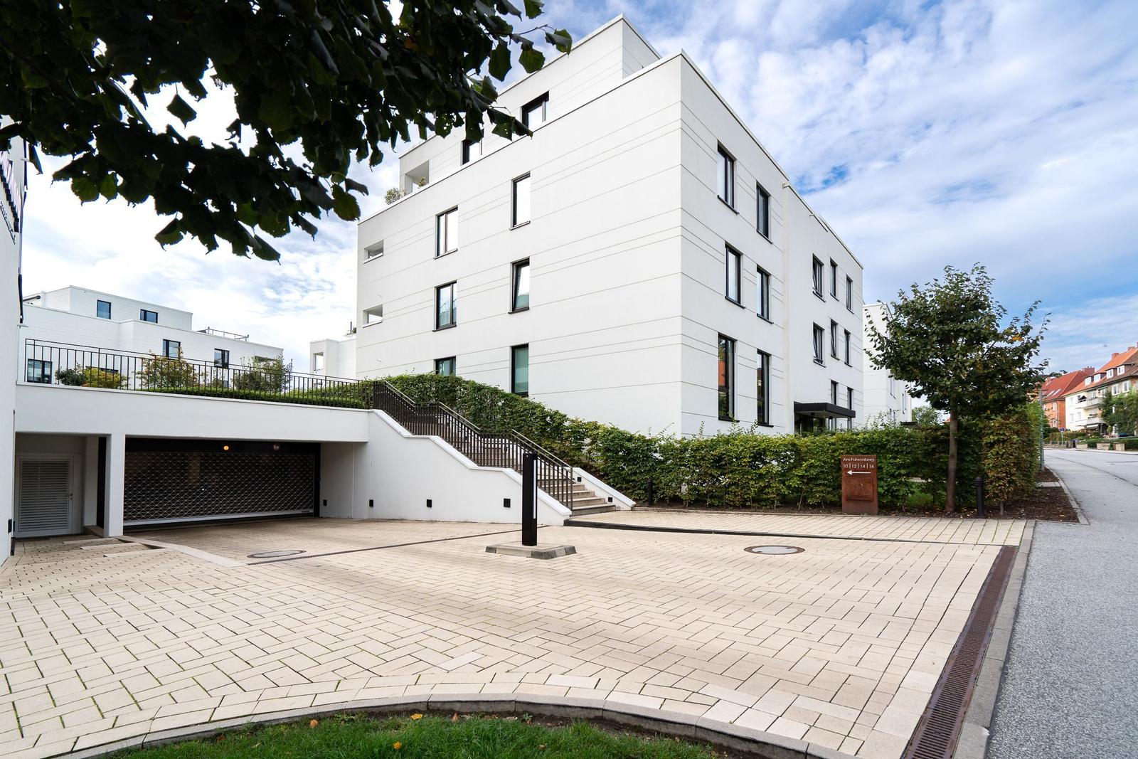 Modernes weißes Mehrfamilienhaus mit gepflastertem Hof und Treppenaufgang.