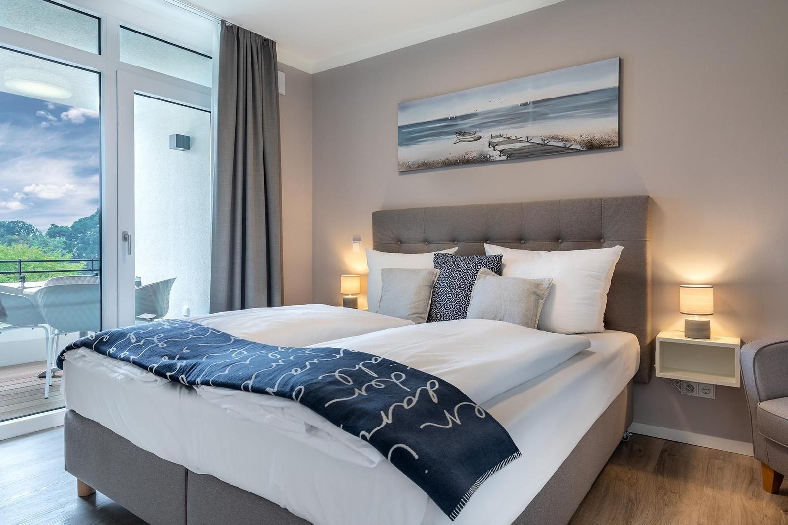 Schlafzimmer mit Balkon, Bett und Wandbild.