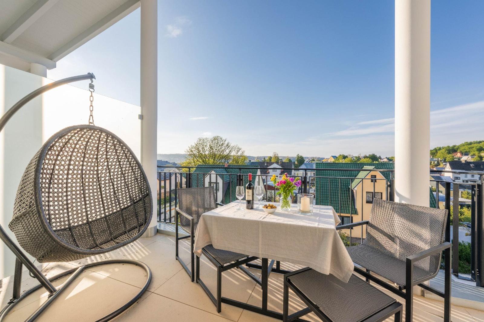 Terrasse mit Tisch, Stühlen und Hängesessel. Blick auf Dächer und Landschaft.