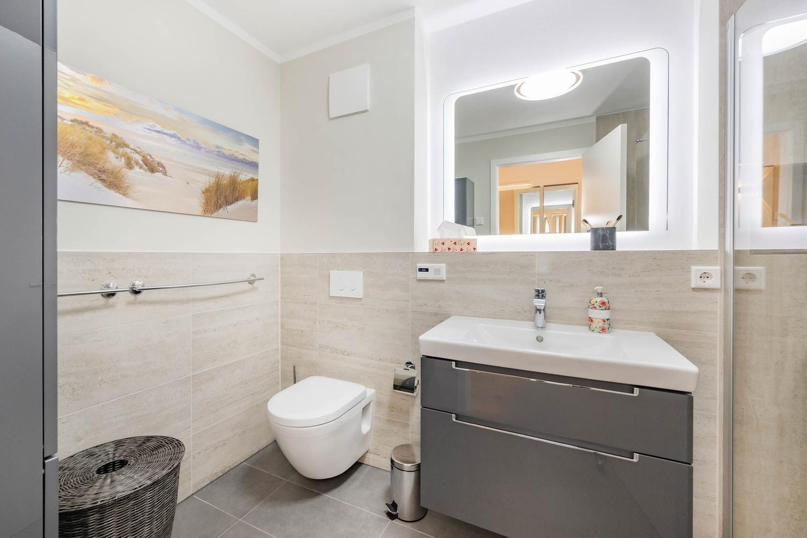 Badezimmer mit Waschbecken, Spiegel, Toilette und Dusche.