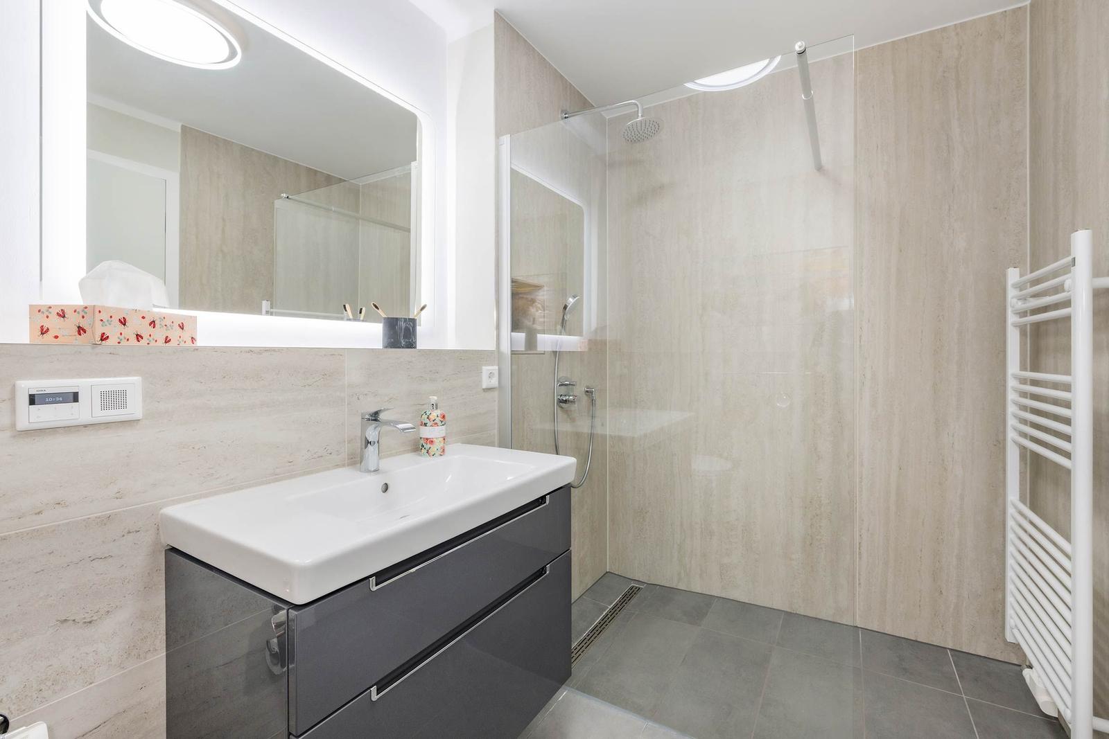 Badezimmer mit Dusche, Waschbecken und Spiegel.