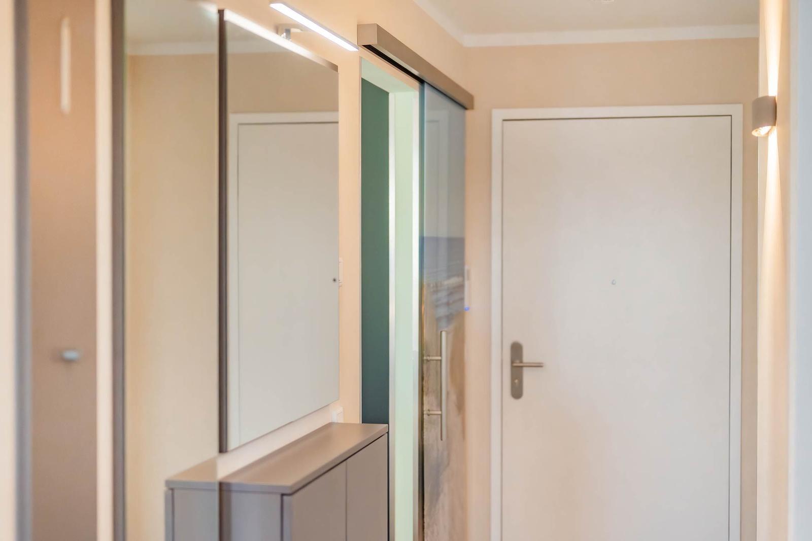 Hausgang mit Spiegelschrank, Glastür und weißer Tür mit Griff.