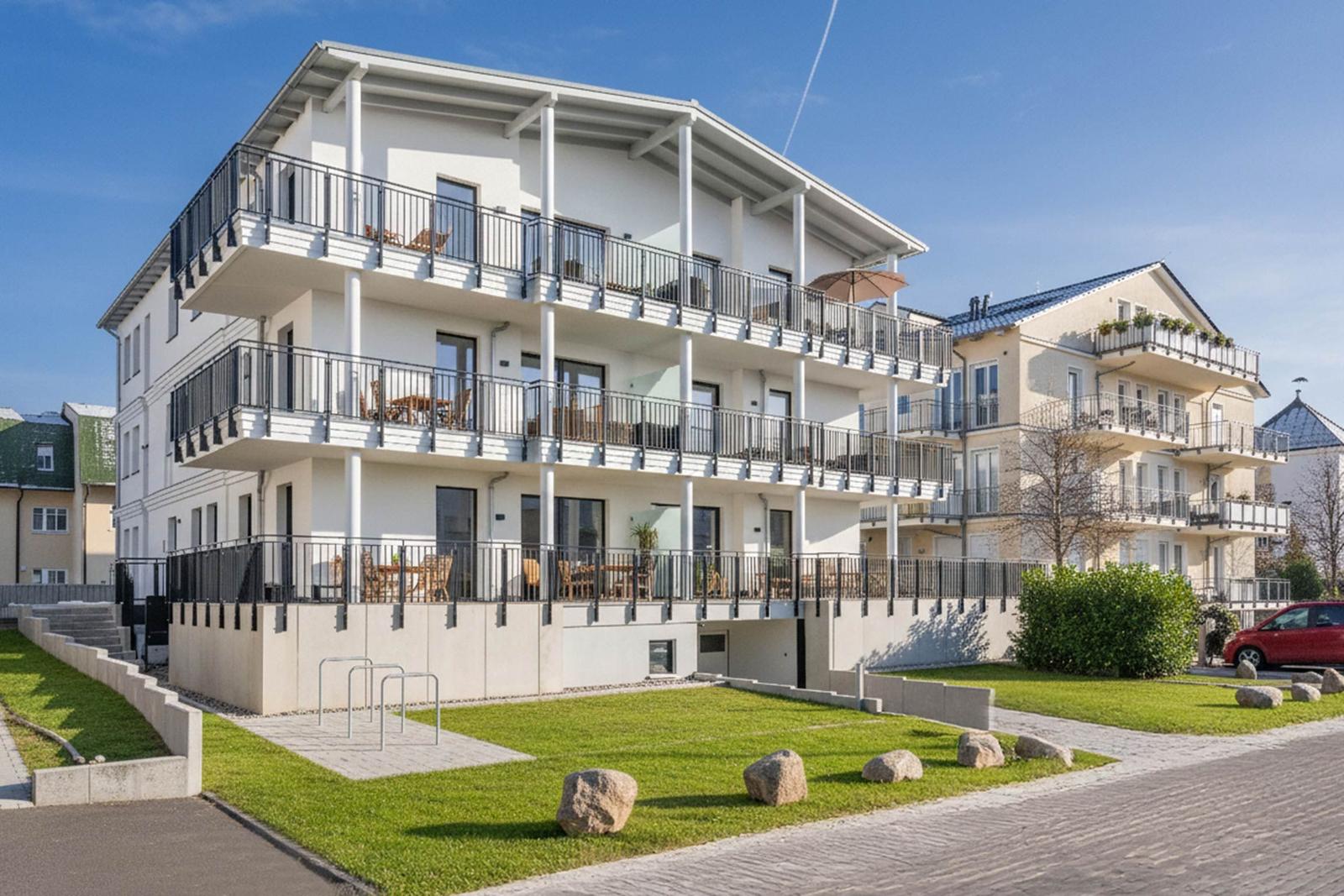 Modernes Mehrfamilienhaus mit Balkonen und Grünfläche.