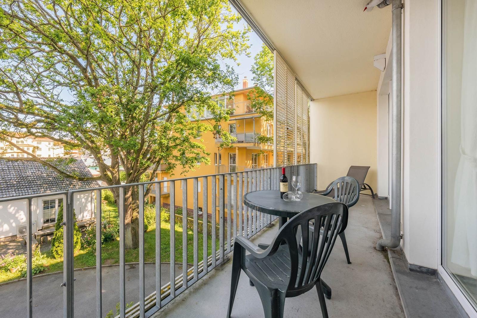 Terrasse mit Tisch, Stühlen und Blick auf einen Garten und gelbes Gebäude.
