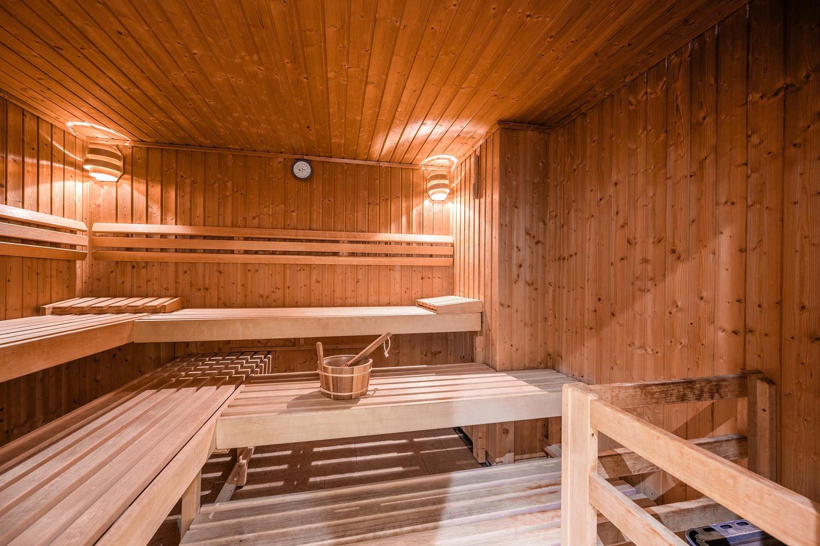Holzsauna mit mehreren Bänken und einem Eimer mit Löffel.