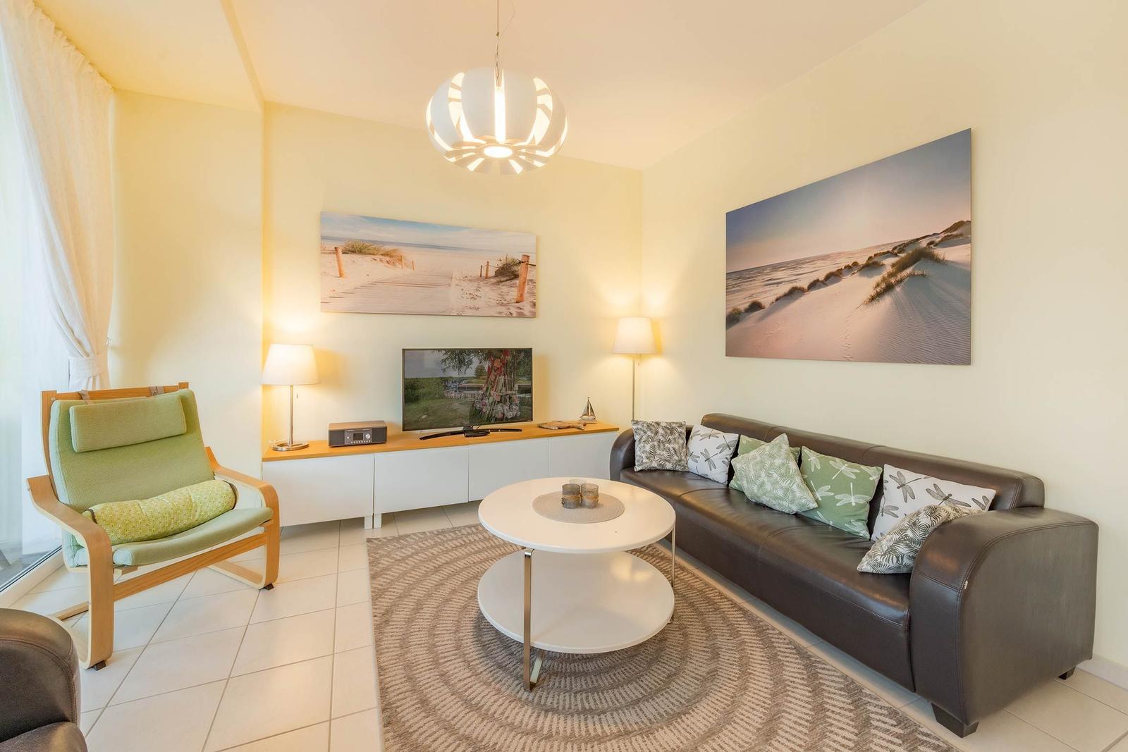 Wohnzimmer mit Sofa, Sessel, Couchtisch und Wandbildern