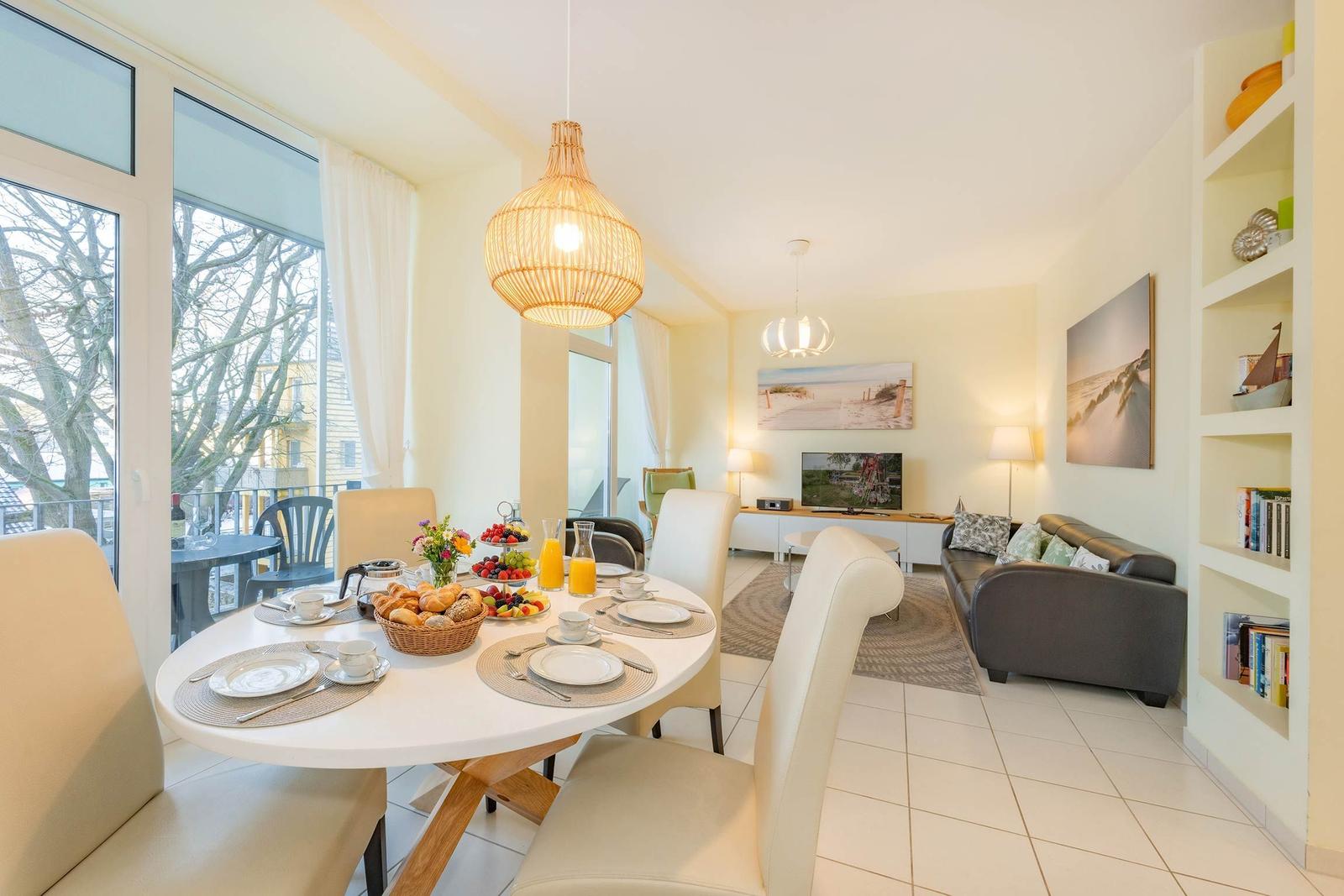 Esszimmer mit Tisch, Stühlen und Blick auf Balkon. Wohnzimmer mit Sofa und Fernseher.