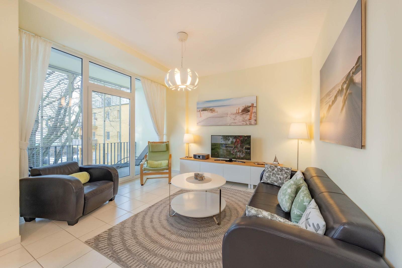 Wohnzimmer mit Sofa, Sessel und TV. Durchgang zur Terrasse.