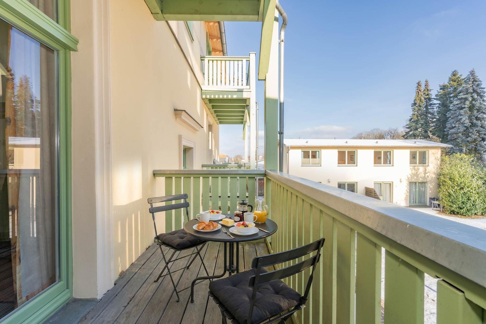 Terrasse mit Tisch und Stühlen, Frühstückszubehör und Blick auf Gebäude und Bäume.