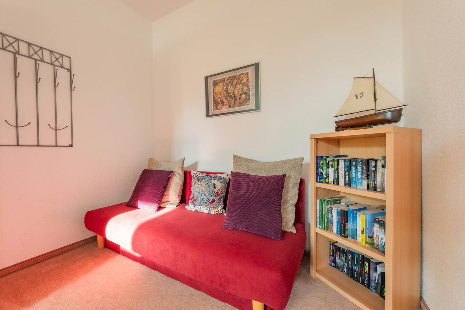 Rotes Sofa mit Kissen, Bücherregal und Segelschiffmodell an der Wand.