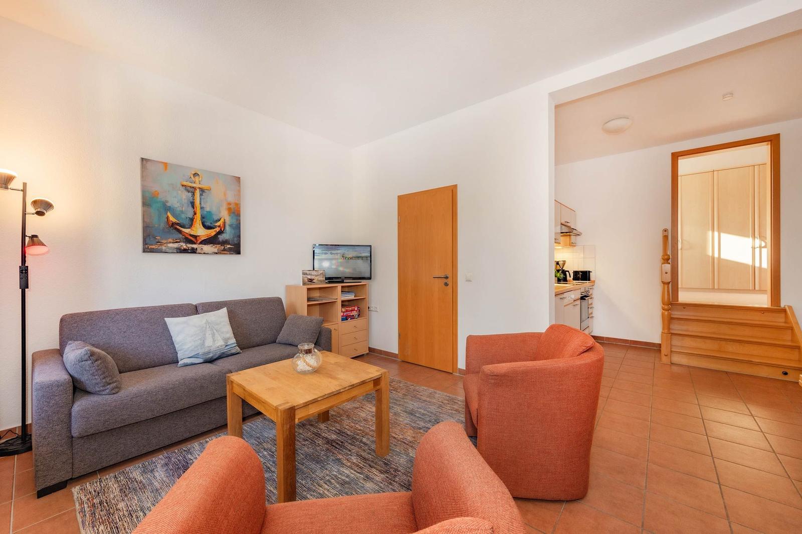 Wohnbereich mit Sofa, zwei Sesseln, Couchtisch und Küchenbereich im Hintergrund.
