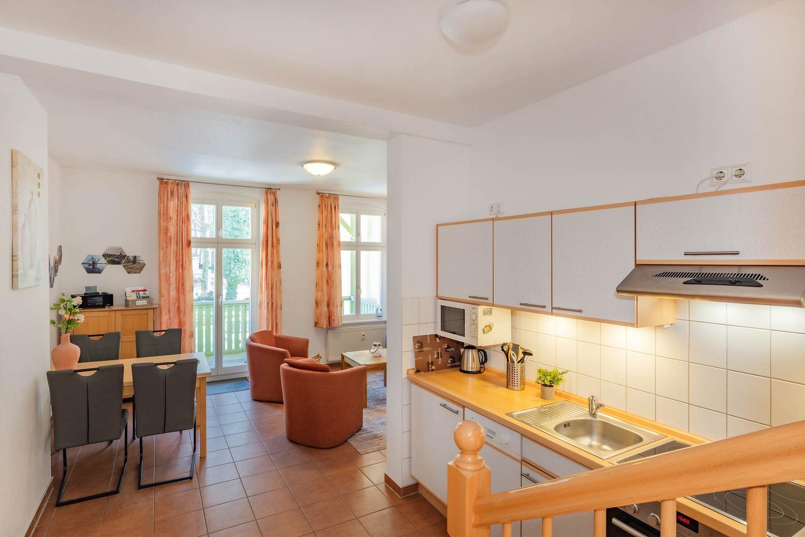 Küche mit Arbeitsfläche, Spüle und Dunstabzug. Wohnbereich mit Tisch, Stühlen und Sesseln.