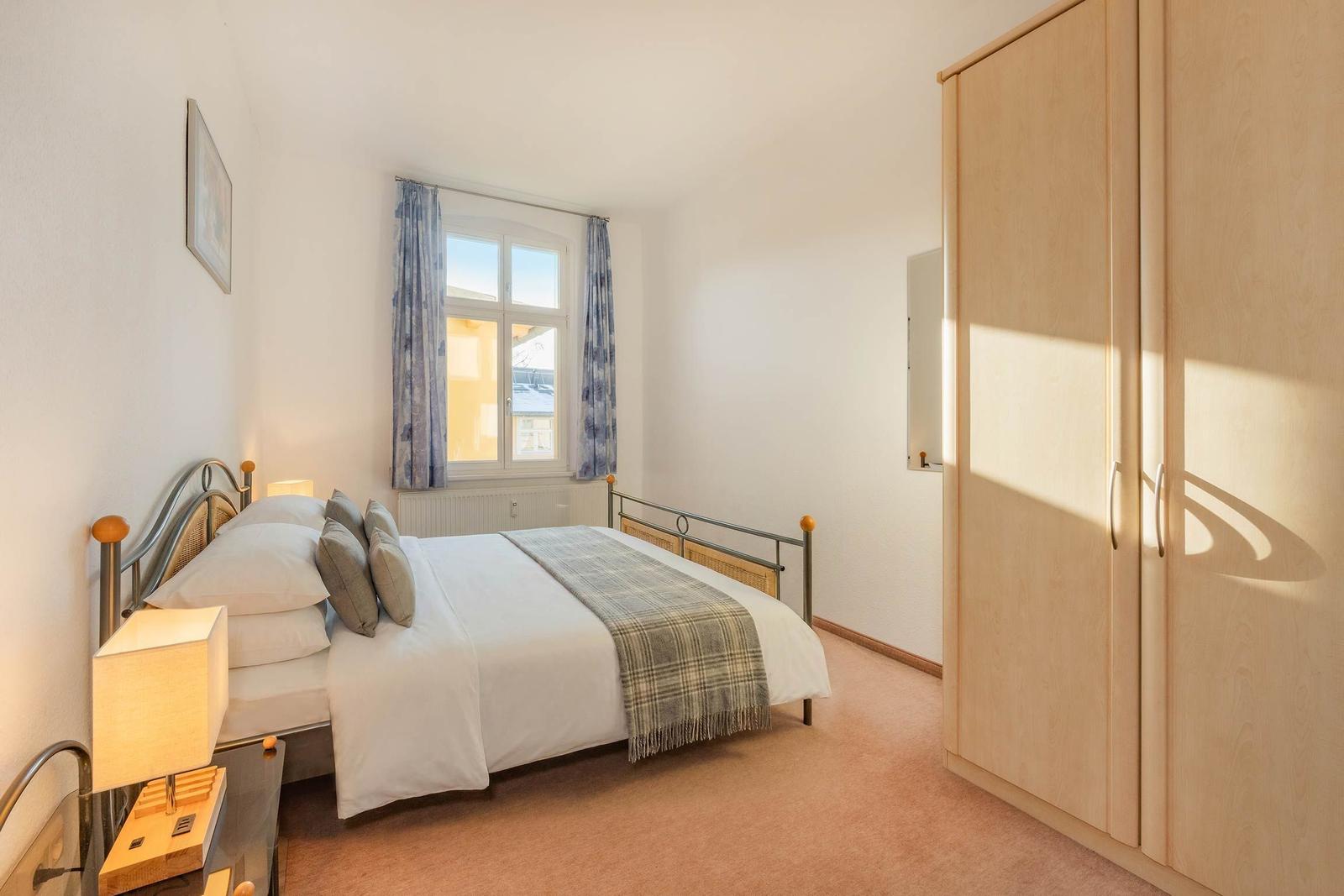 Schlafzimmer mit Bett, Kleiderschrank und Fenster mit Vorhängen.
