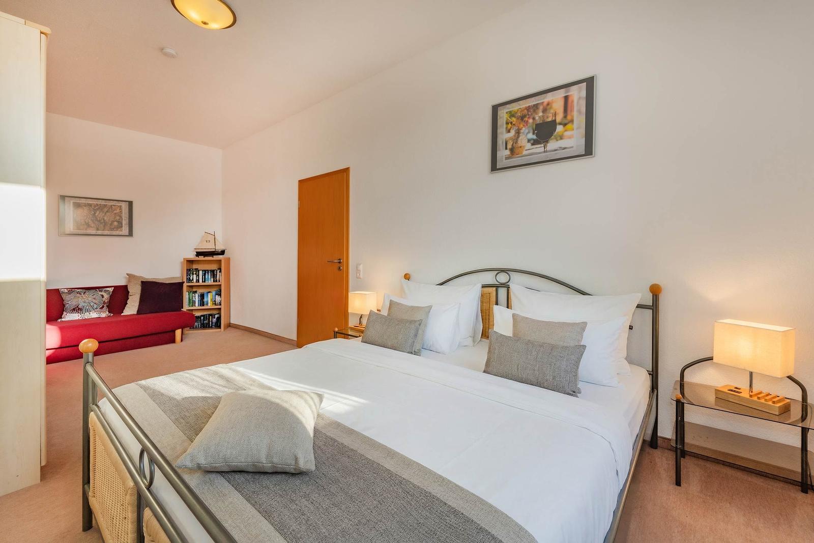 Schlafzimmer mit Doppelbett, Nachttisch und rotem Sofa im Hintergrund.