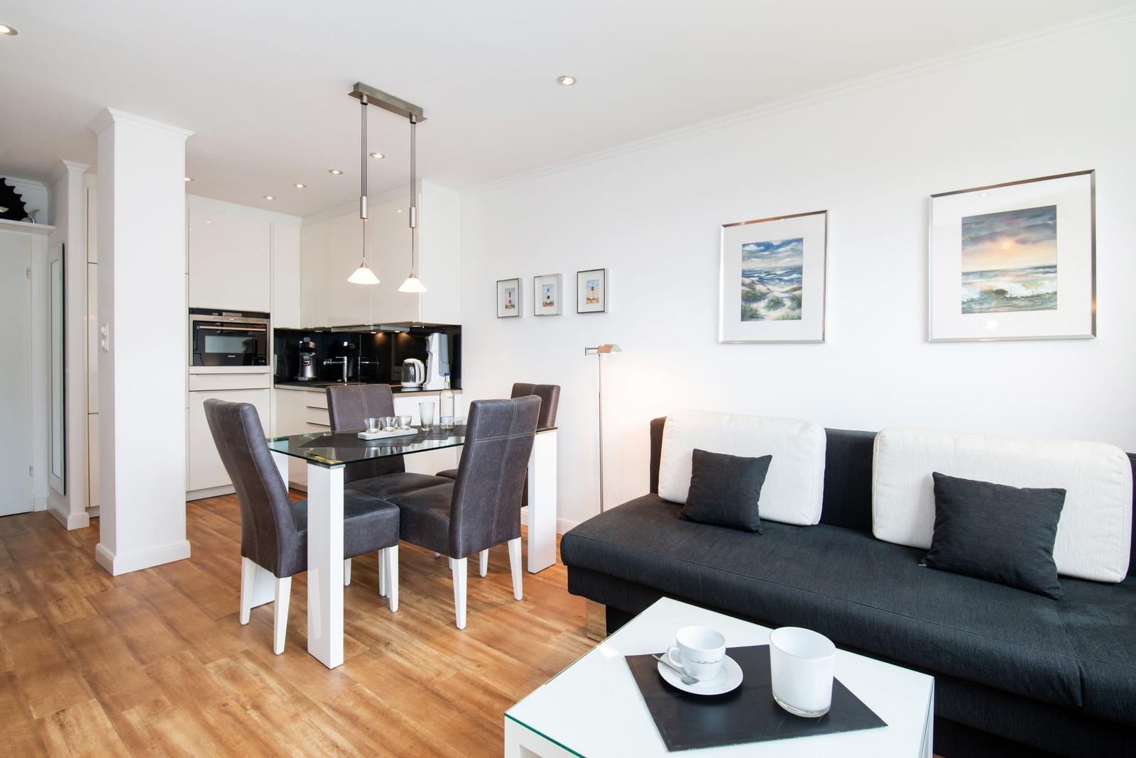 Wohn- und Essbereich mit Sofa, Esstisch und Küche im Hintergrund.