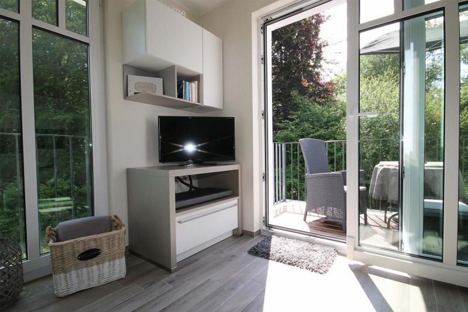 Ein Raum mit TV, Schrank und Balkonansicht durch Glastüren.