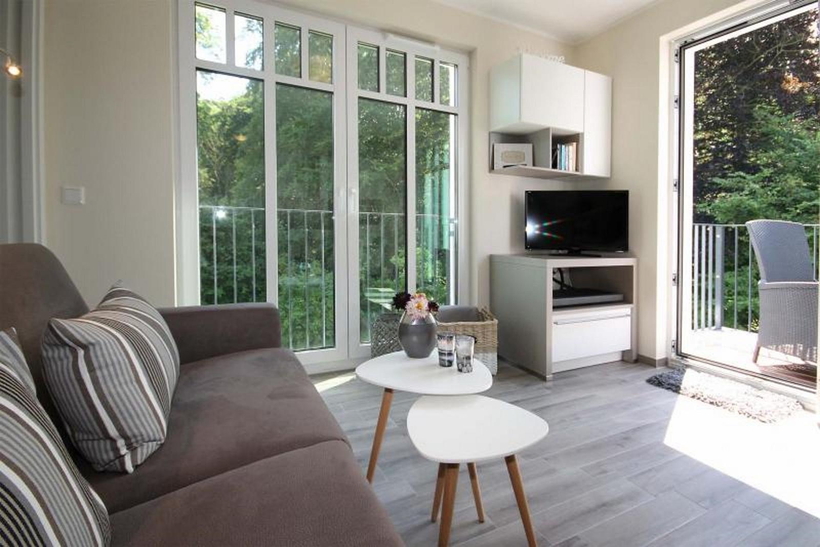 Wohnzimmer mit Sofa, Tischen und TV. Durchgang zur Terrasse mit Blick auf Grün.