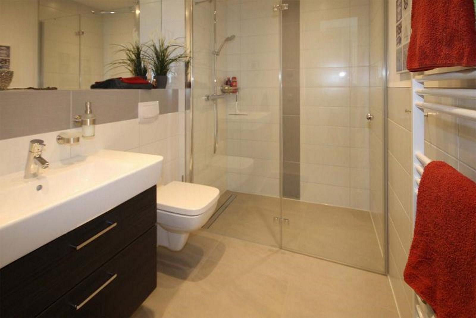 Badezimmer mit Dusche, Waschbecken und Toilette. Rote Handtücher hängen an einem Wärmegerät.