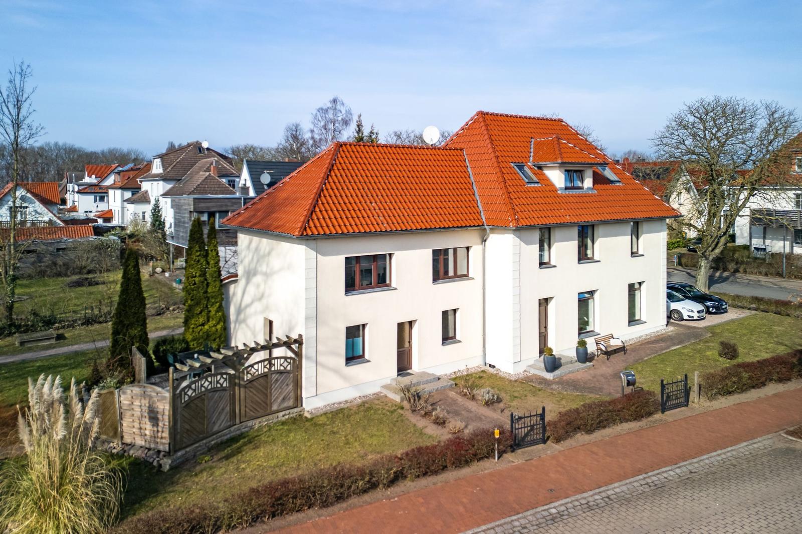Modernes Haus mit rotem Dach und gepflegtem Garten. Parkplätze vor dem Haus.