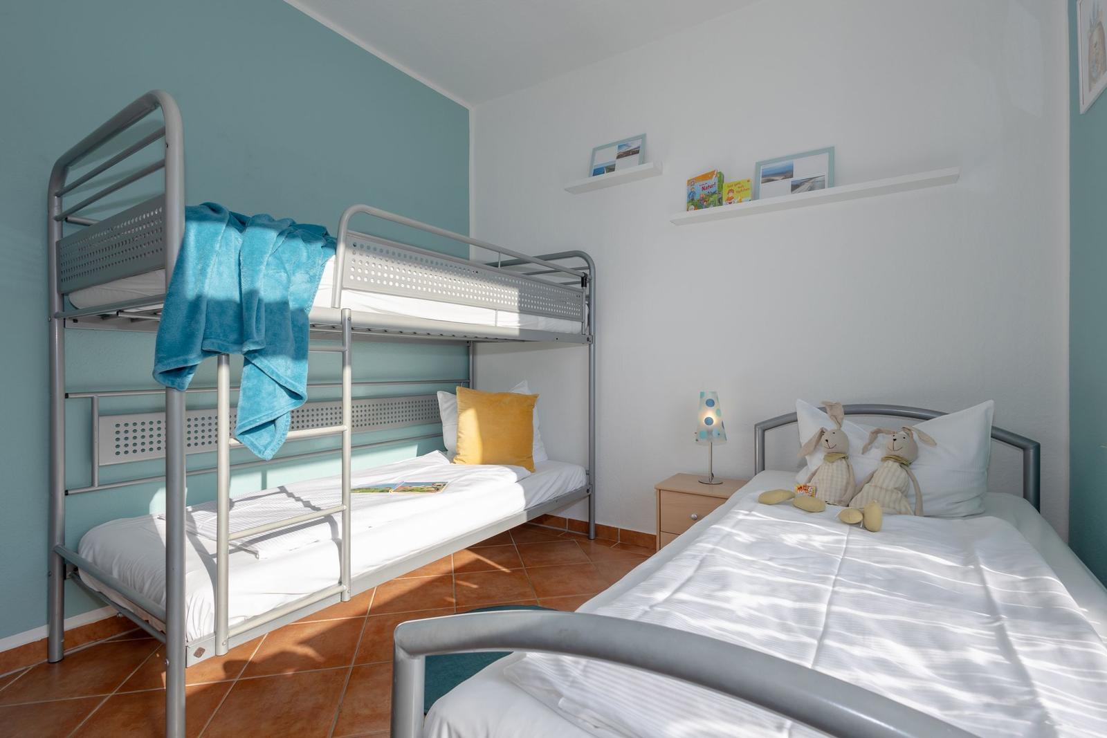 Zimmer mit Doppelstockbett und Einzelbett, Wandregal mit Büchern und Stofftieren.