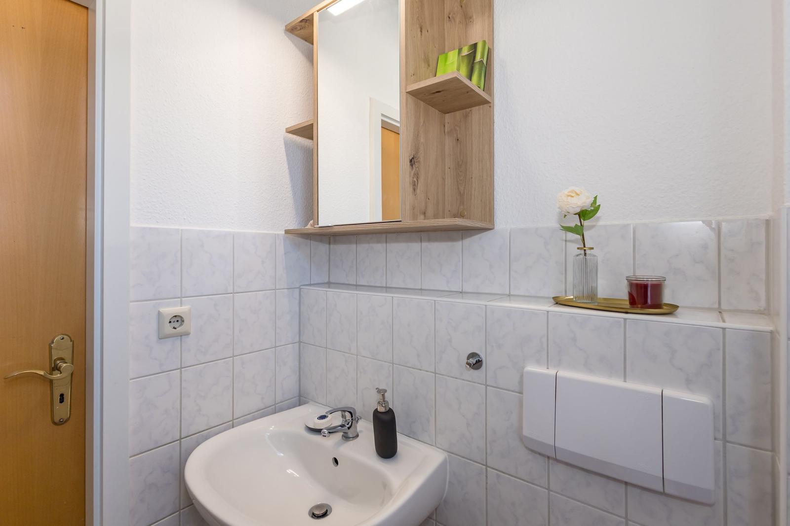 Badezimmer mit Waschbecken, Spiegelschrank und Keramikfliesen.