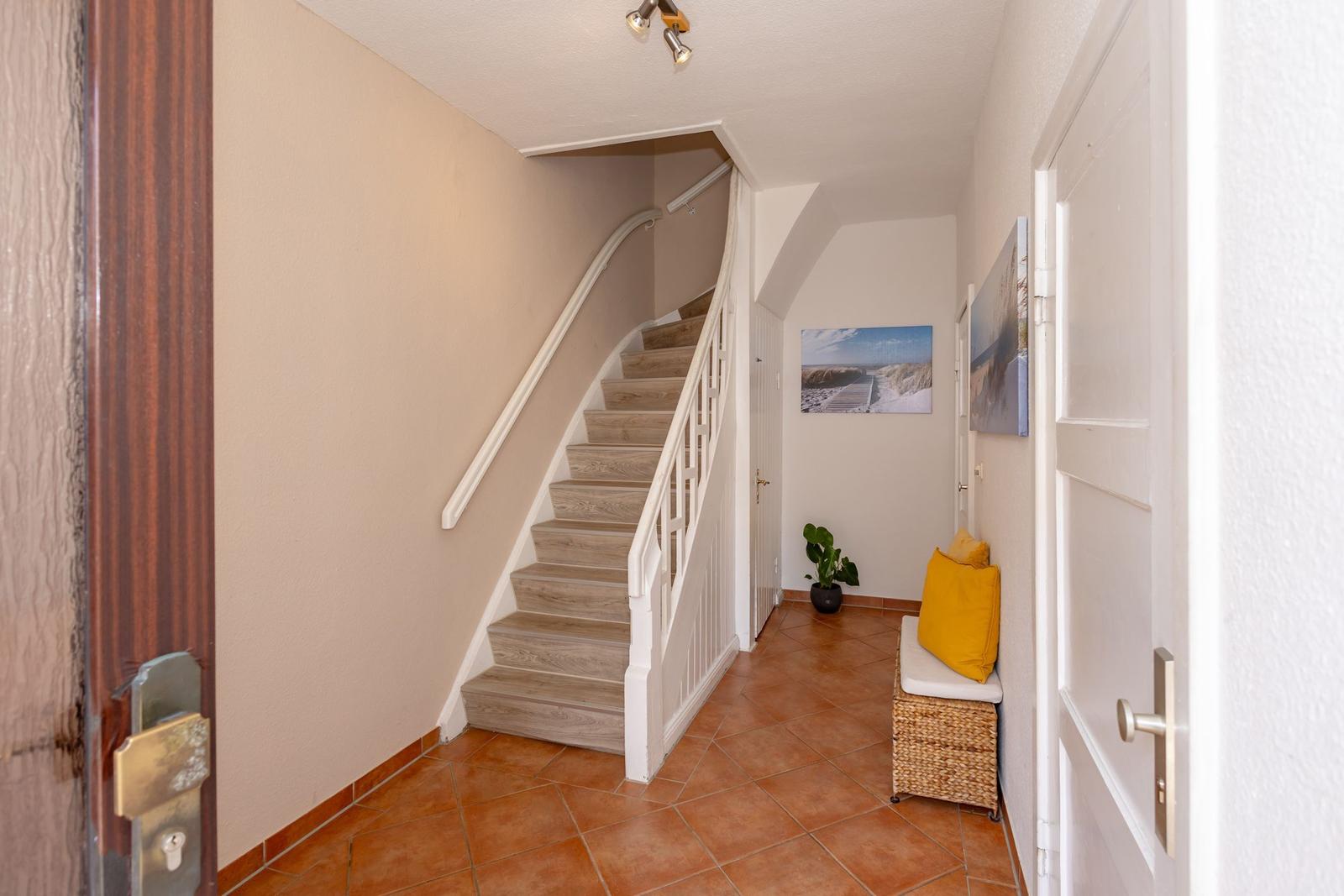 Hausflur mit Treppe, Sitzbank und Wandbildern.