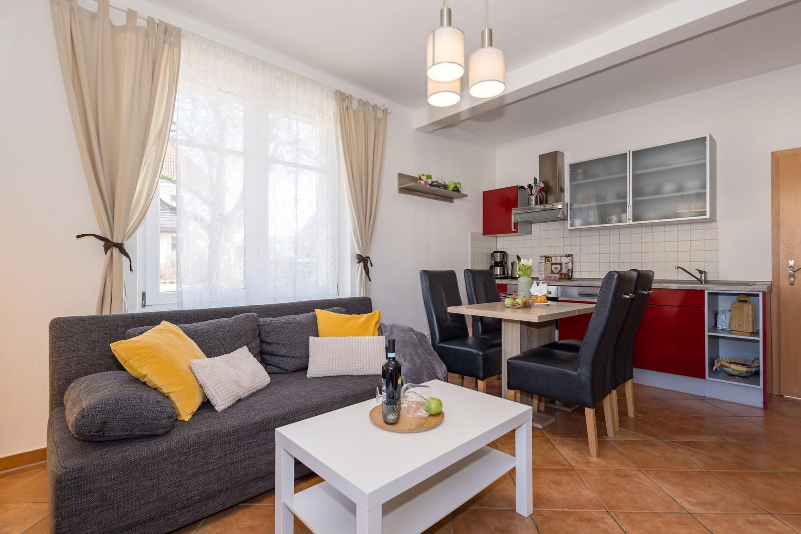 Wohn- und Küchenbereich mit Sofa, Tisch und roten Schränken.