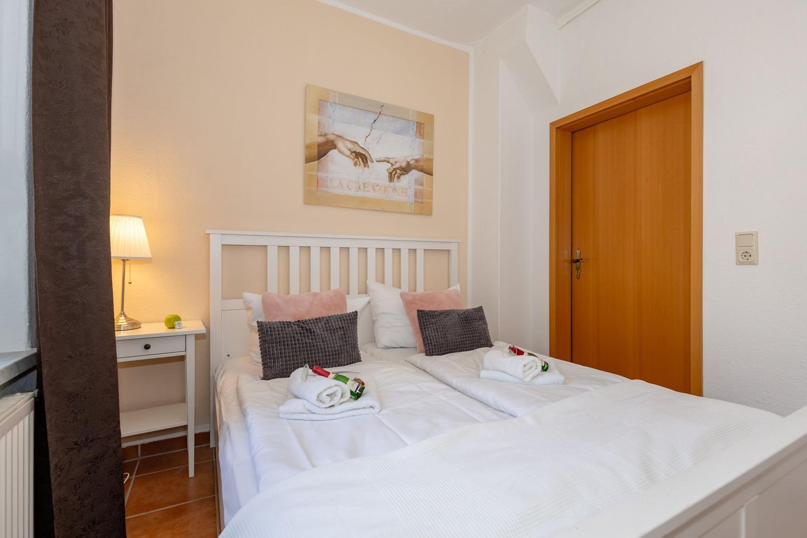 Schlafzimmer mit Bett, Nachttisch, Lampe und Wandbild.