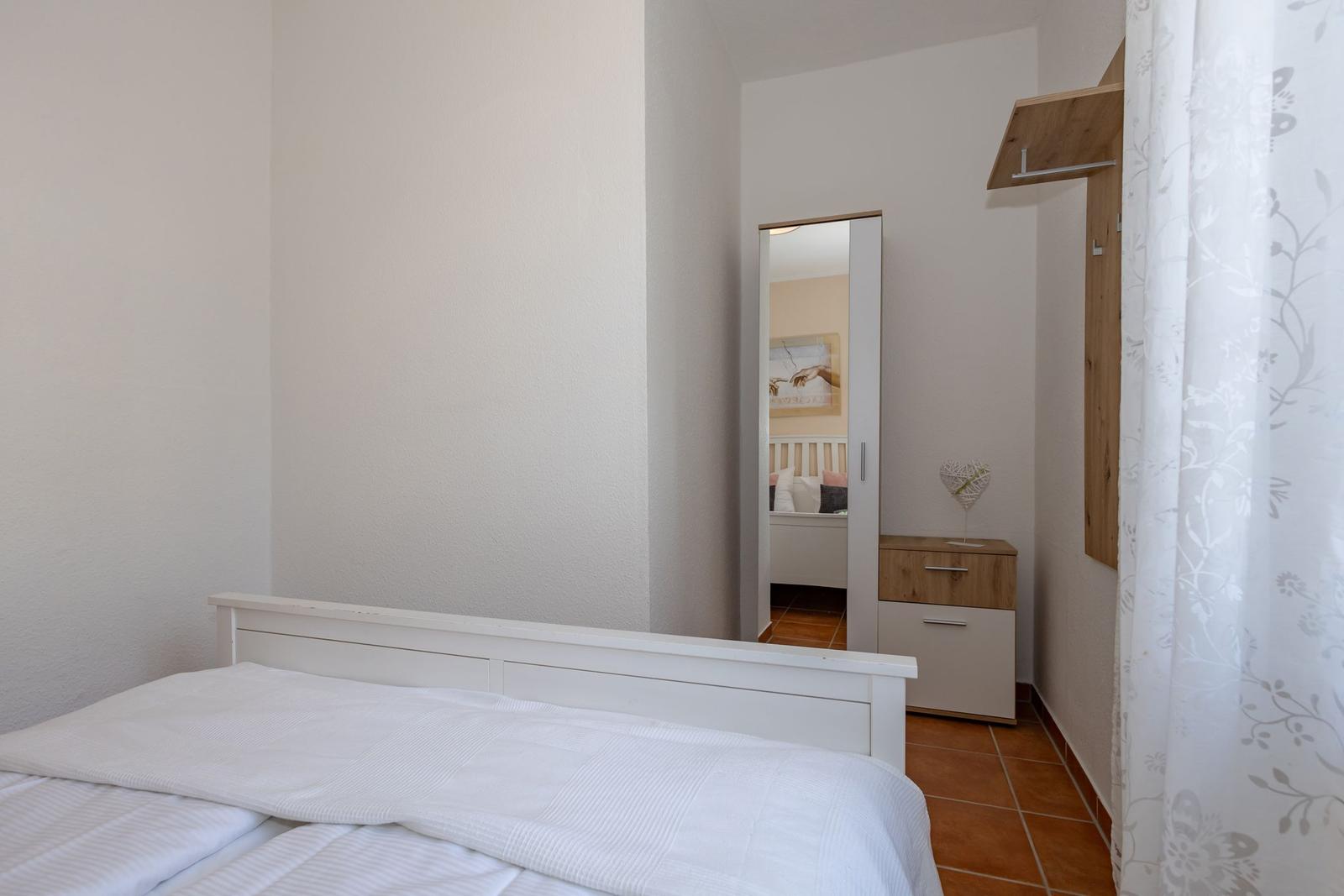 Schlafzimmer mit weißem Bett, Spiegelschrank und Holzgarderobe.