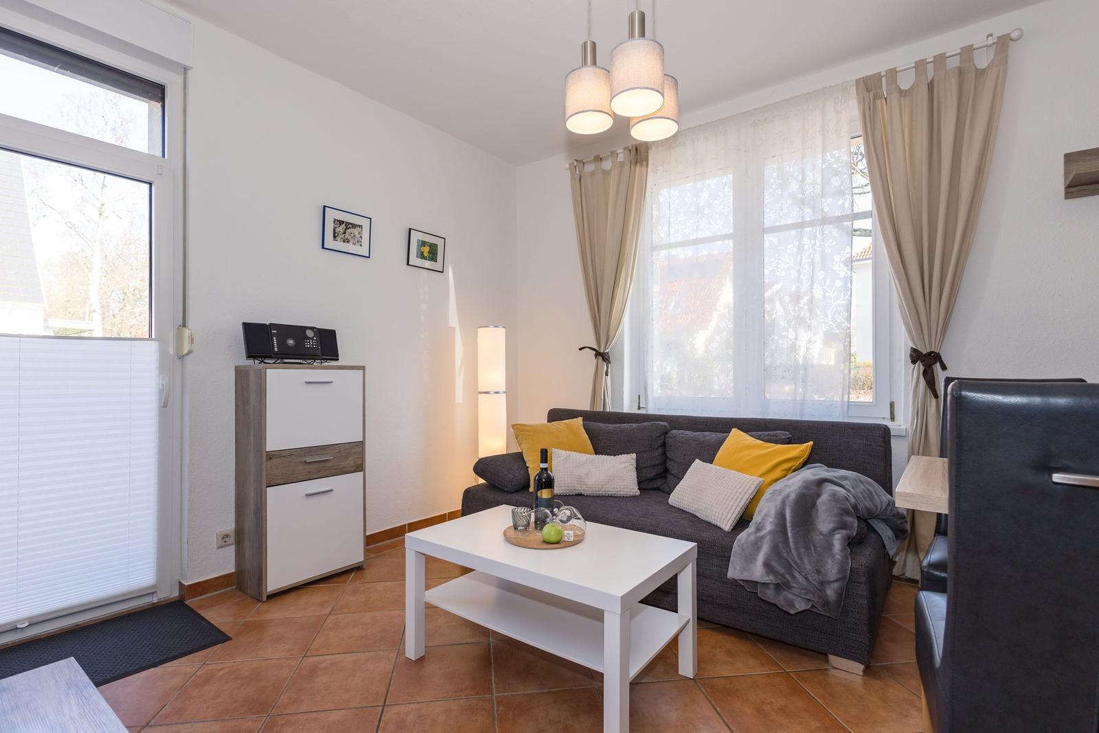 Wohnzimmer mit Sofa, Tisch und Fenstern.
