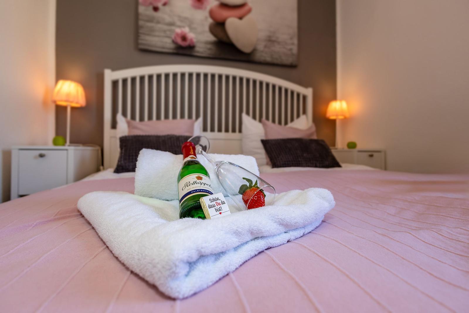 Ein Bett mit rosa Bettwäsche, weißen Kissen und einer Flasche Wein.
