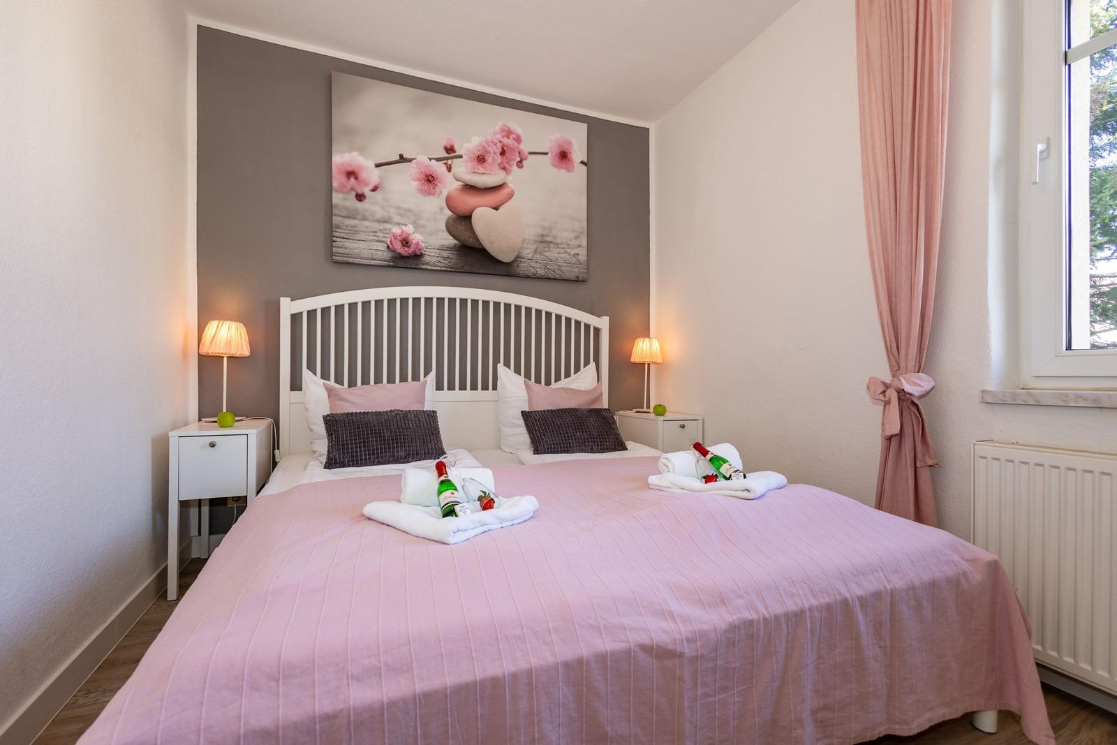 Schlafzimmer mit Bett, Nachttischen und Fenster mit Vorhängen.