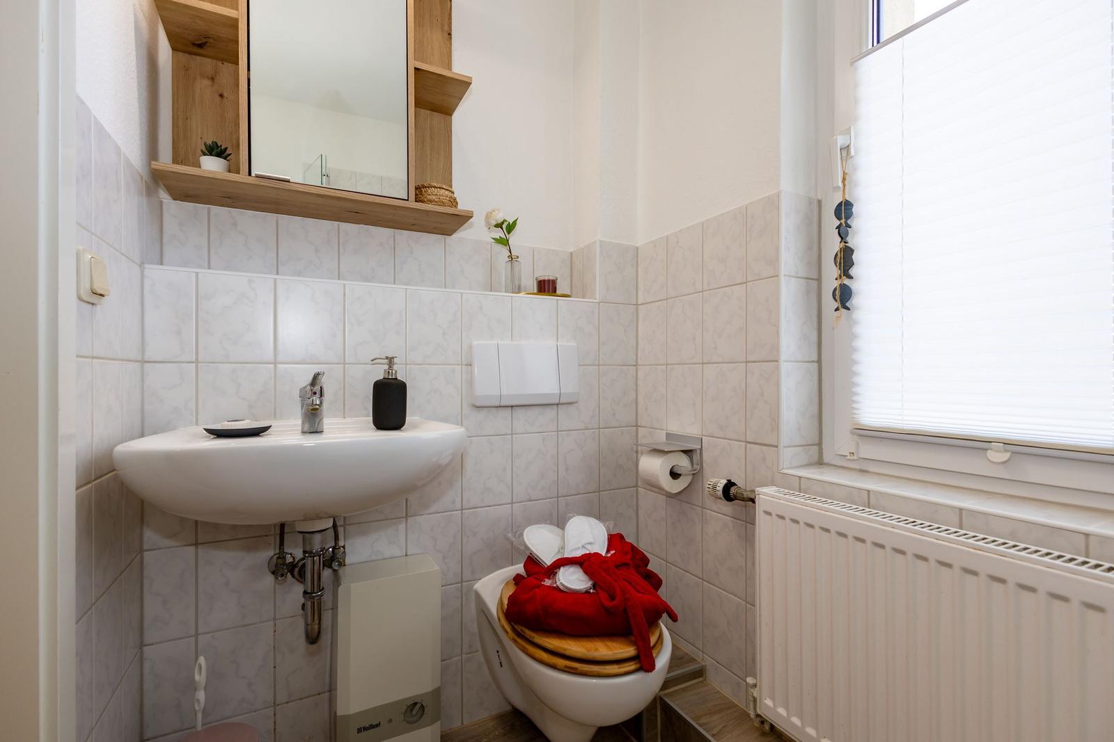 Badezimmer mit Waschbecken, Toilette und Fenster mit Jalousie.
