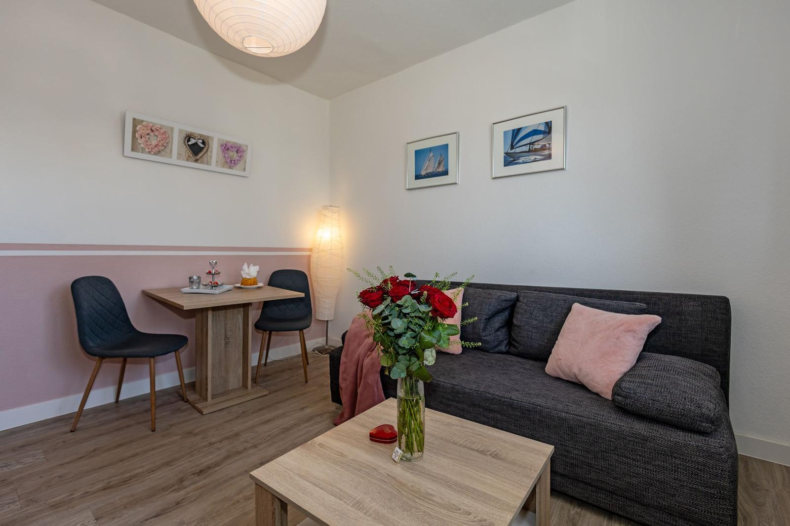 Wohnzimmer mit Sofa, Tisch und Stühlen, Wandbilder und Blumen auf dem Tisch.