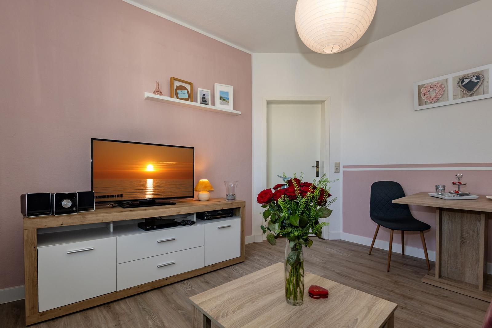 Wohnzimmer mit TV, Schreibtisch und Blumen. Wandfarbe rosa.