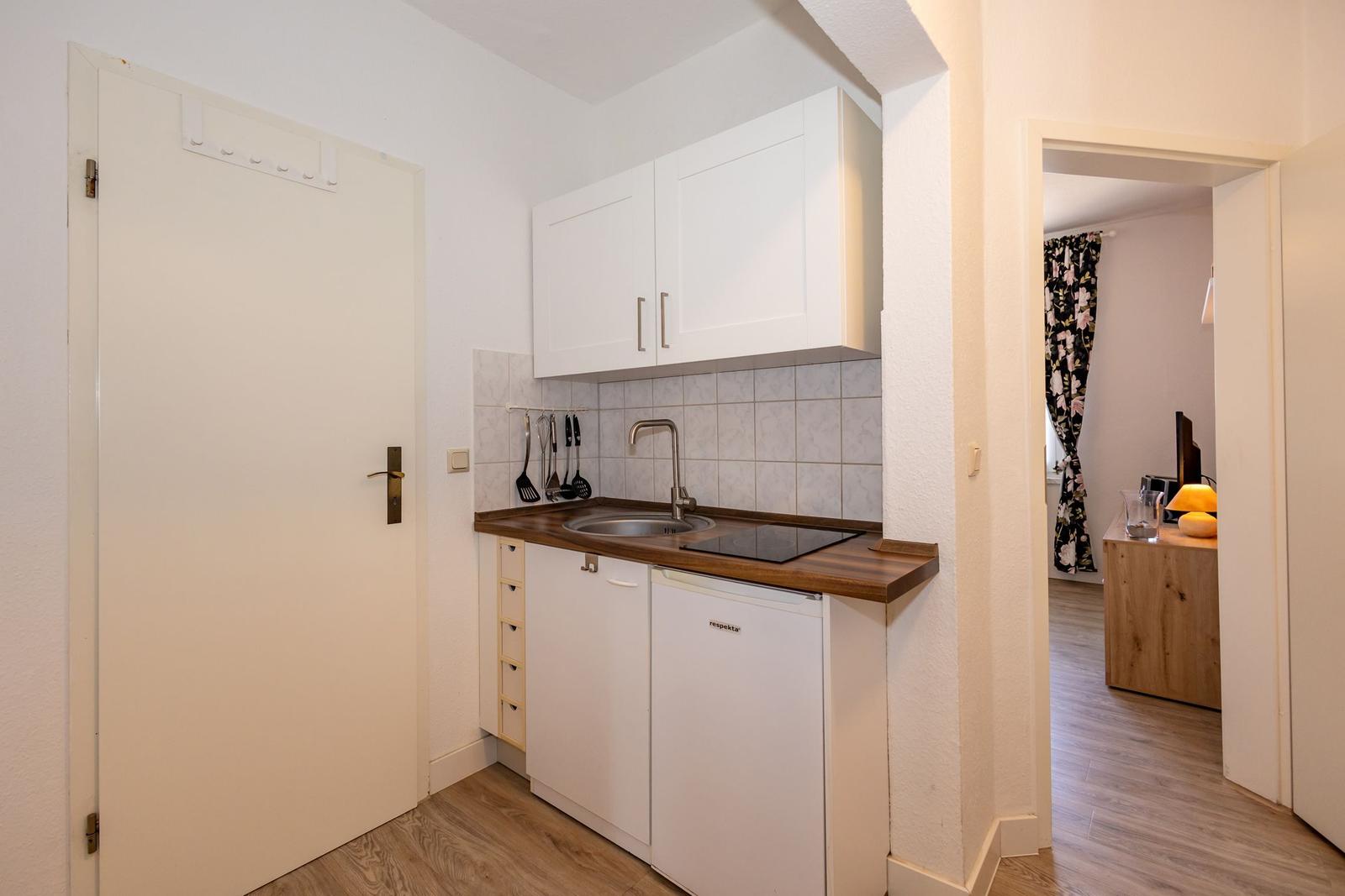 Küche mit Spüle, Herd und Kühlschrank. Tür und Blick in Wohnzimmer.