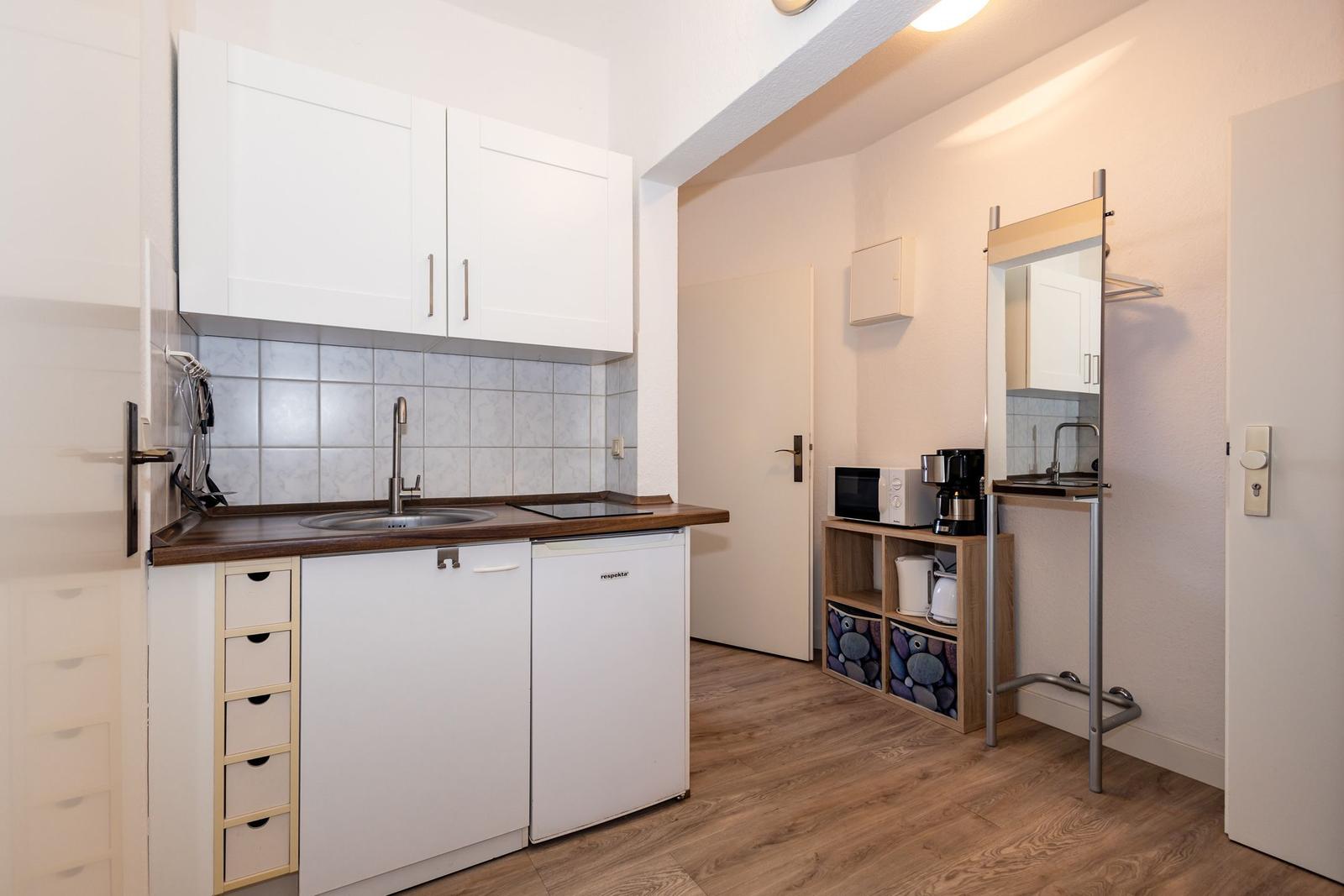 Küche mit Spüle, Kühlschrank und Kochfeld. Nebenraum mit Spiegel und Küchengeräten.