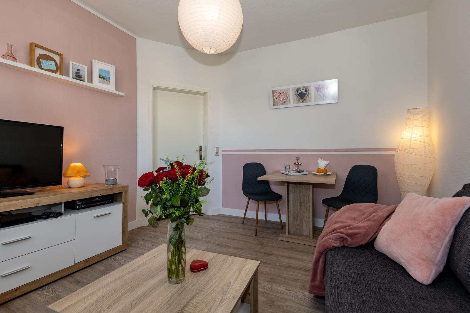 Wohnzimmer mit Sofa, Esstisch, Fernseher und Blumen.