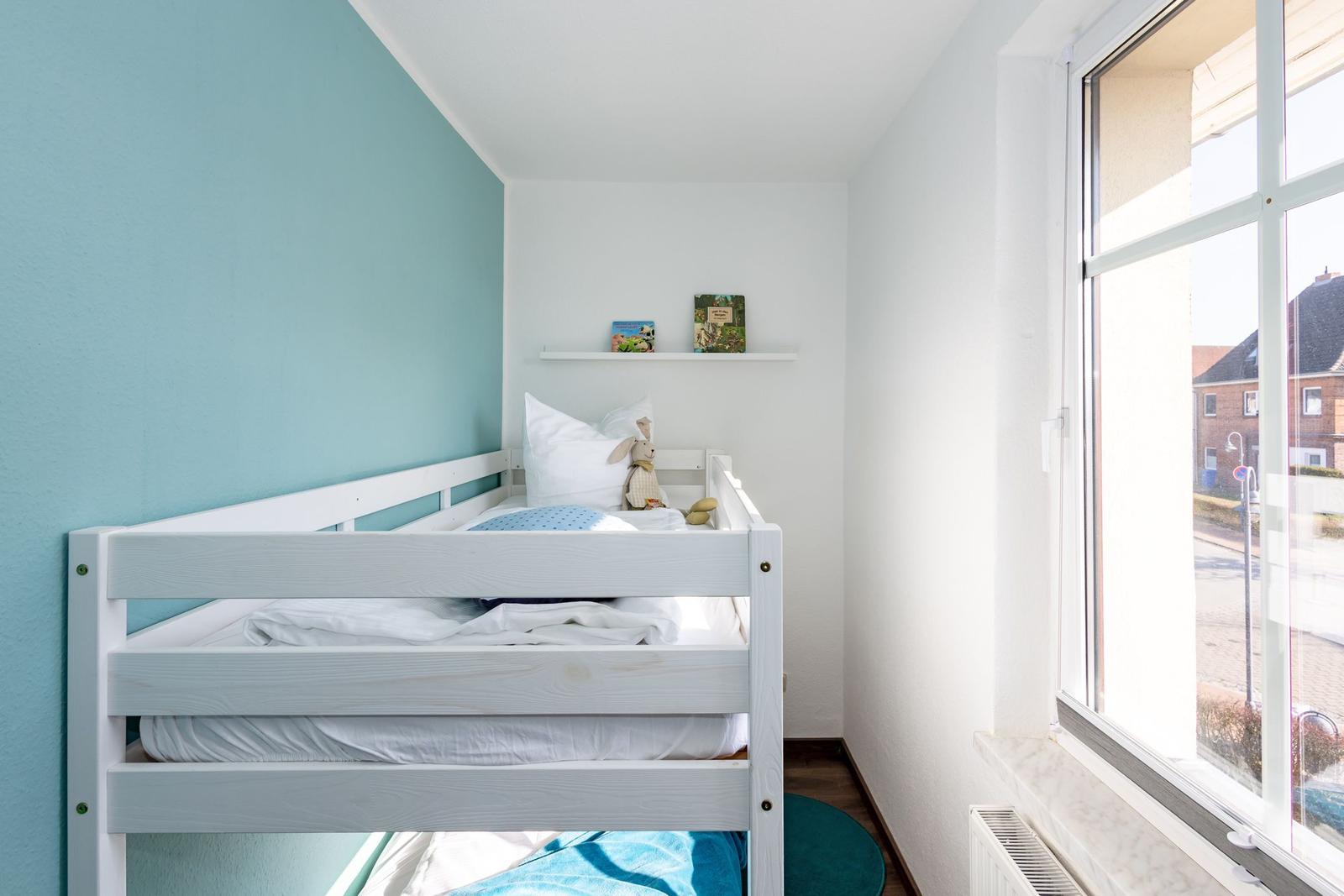 Ein Schlafzimmer mit Doppelbett, Fenster und Bücherregal.