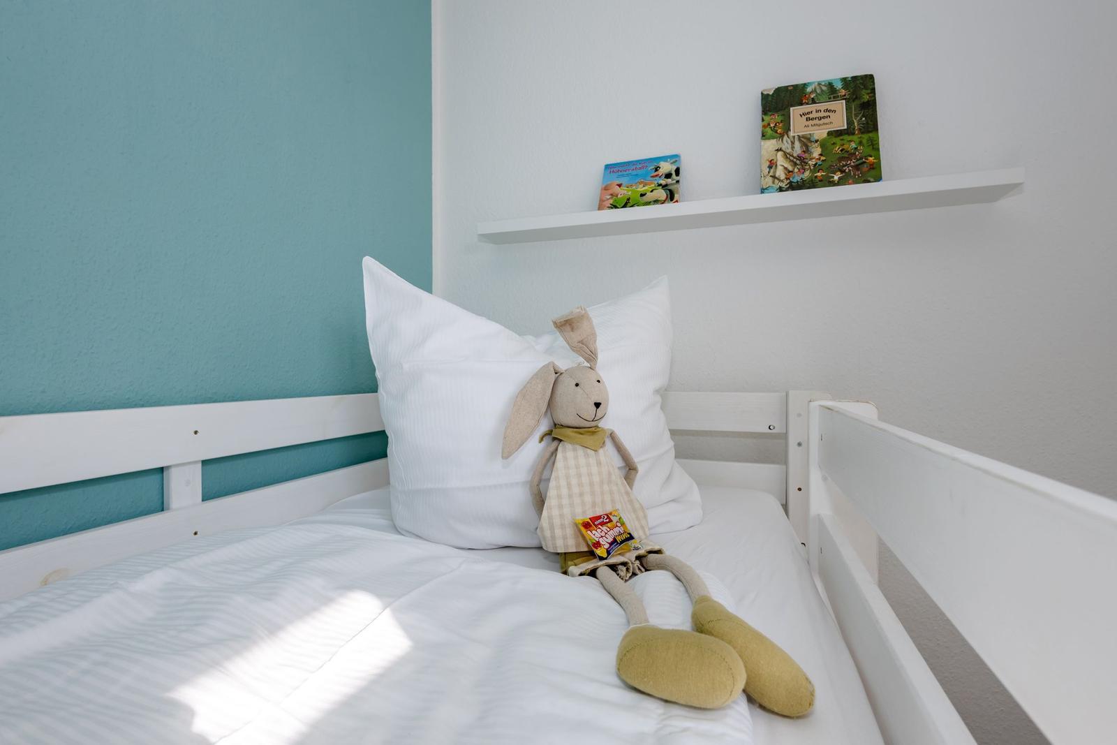 Ein Kinderbett mit Kissen, Stofftier und Büchern auf Regal.