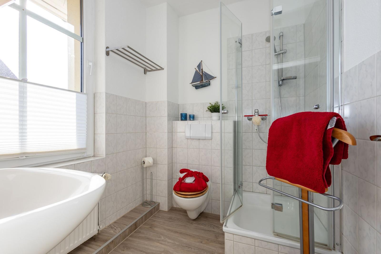 Badezimmer mit Badewanne, Dusche und Toilette. Rote Handtücher und Segelschiff-Dekoration.