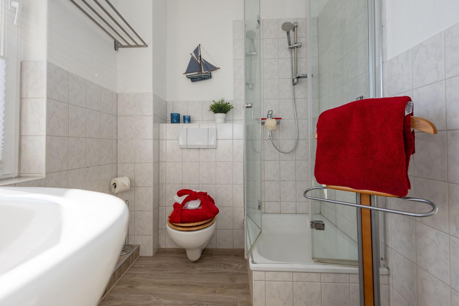 Badezimmer mit Dusche, Toilette und Badewanne. Rote Handtücher und Schiffsmotiv.