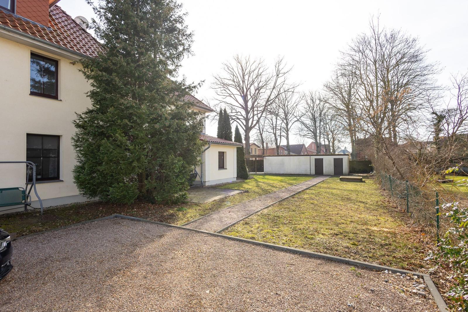 Haus mit Garten, Kiesfläche und Bäumen. Nebengebäude und Weg sind sichtbar.