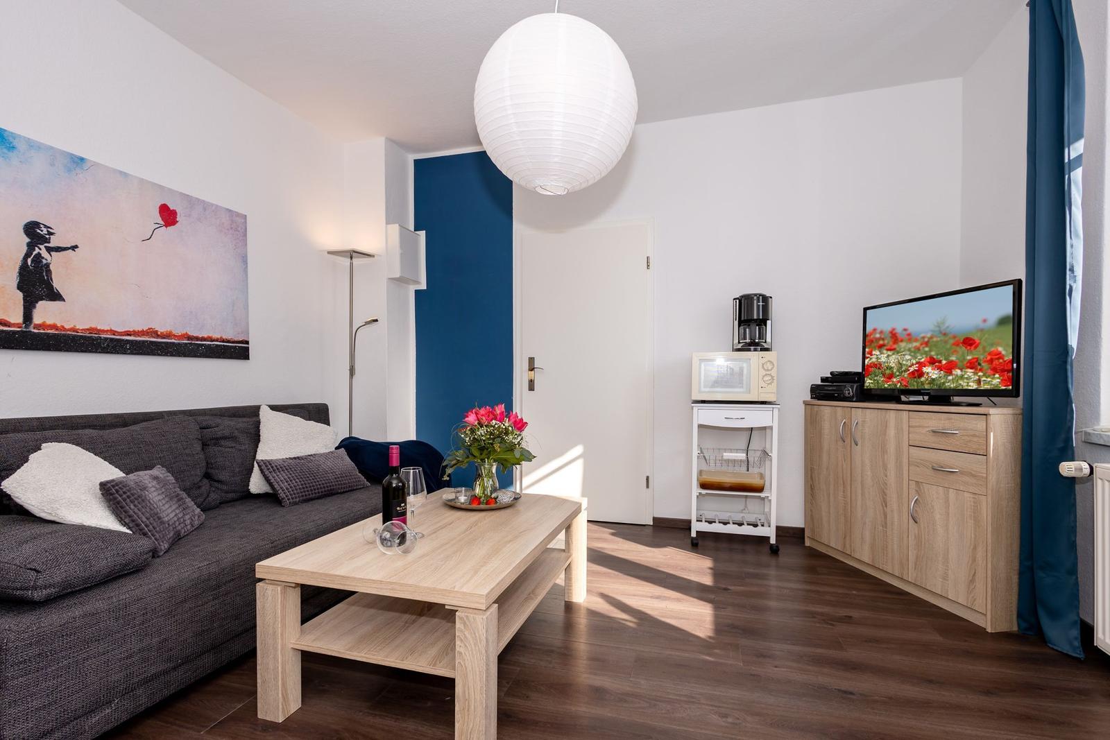 Wohnzimmer mit Sofa, Couchtisch, Fernseher und Küchenzeile.