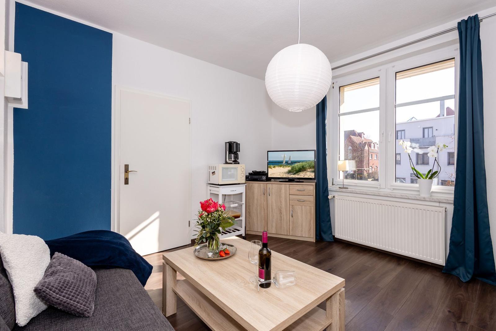 Wohnzimmer mit Sofa, Couchtisch und Fernseher. Fenster mit Blick auf Stadt.