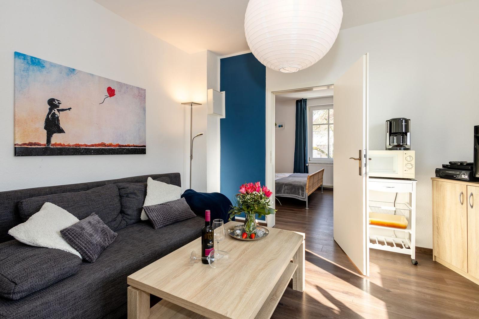 Wohnzimmer mit Sofa, Couchtisch und Gemälde. Durchgang zur Schlafzimmer.