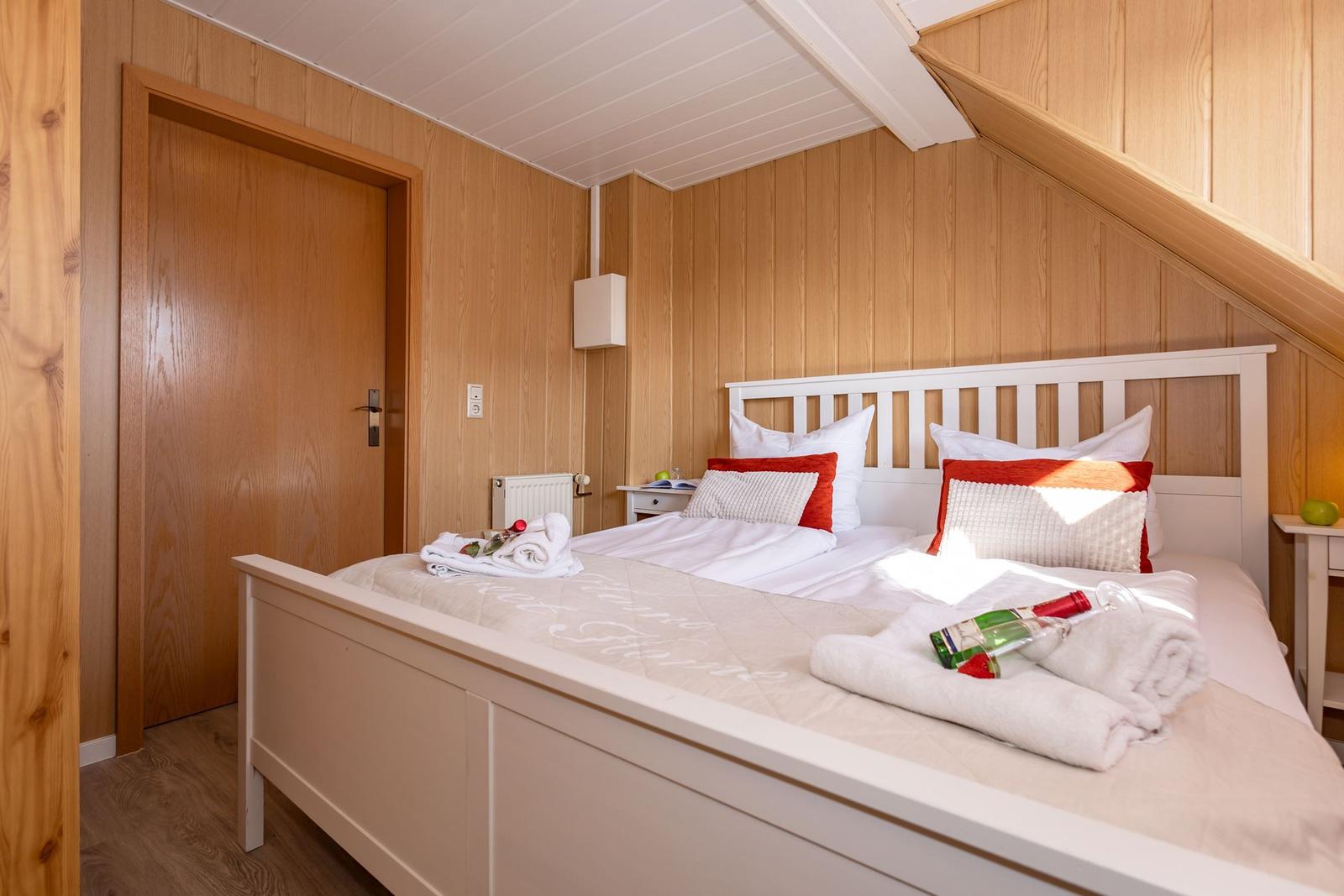 Schlafzimmer mit Holzwänden, weißem Bett und roten Kissen.