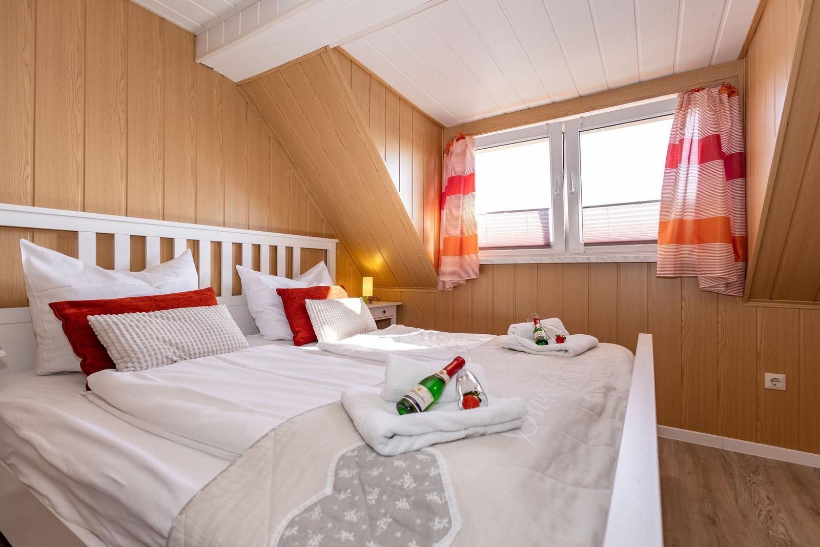 Schlafzimmer mit Dachschrägen, Bett mit Kissen und Flaschen auf Handtüchern.