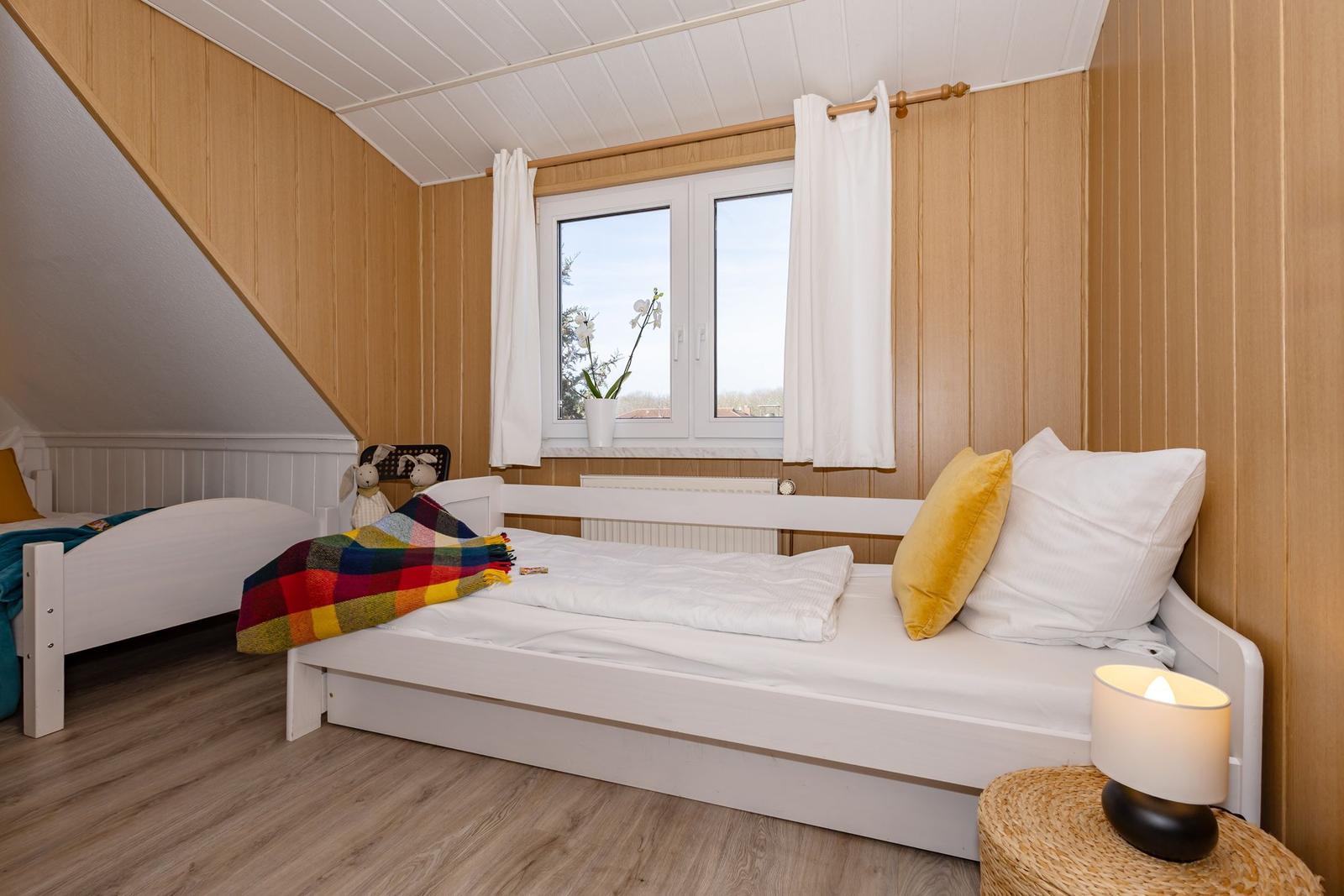 Zwei Betten mit weißen Laken und bunten Decken unter Holzwänden und Dachschrägen.