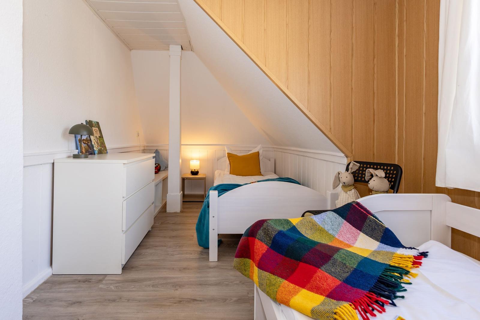 Zwei Betten unter Dachschrägen mit Holzwand und Schrank.